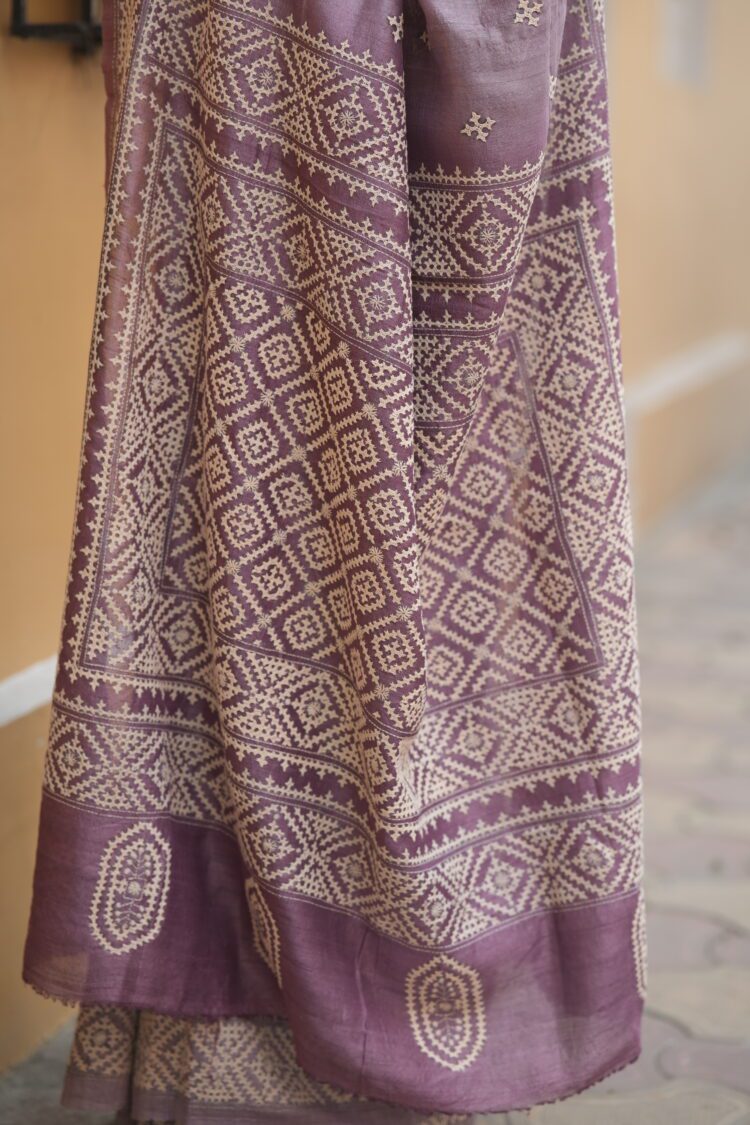 Close-up of beige Gujarati thread work and traditional hand embroidery on a textured mauve Tussar silk fabric.