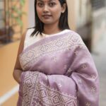 Close-up of beige Gujarati thread work and traditional hand embroidery on a textured mauve Tussar silk fabric.