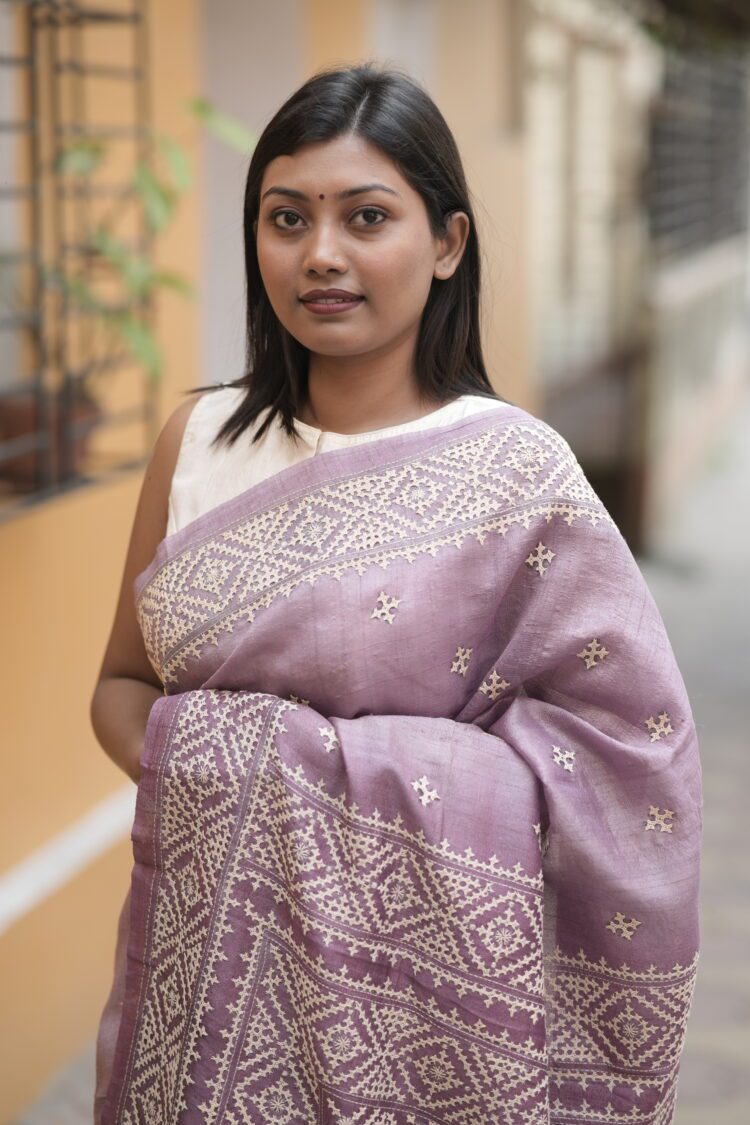 Close-up of beige Gujarati thread work and traditional hand embroidery on a textured mauve Tussar silk fabric.